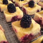 lemon blackberry cheesecake bars on a wire rack.