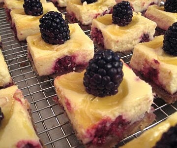lemon blackberry cheesecake bars on a wire rack.
