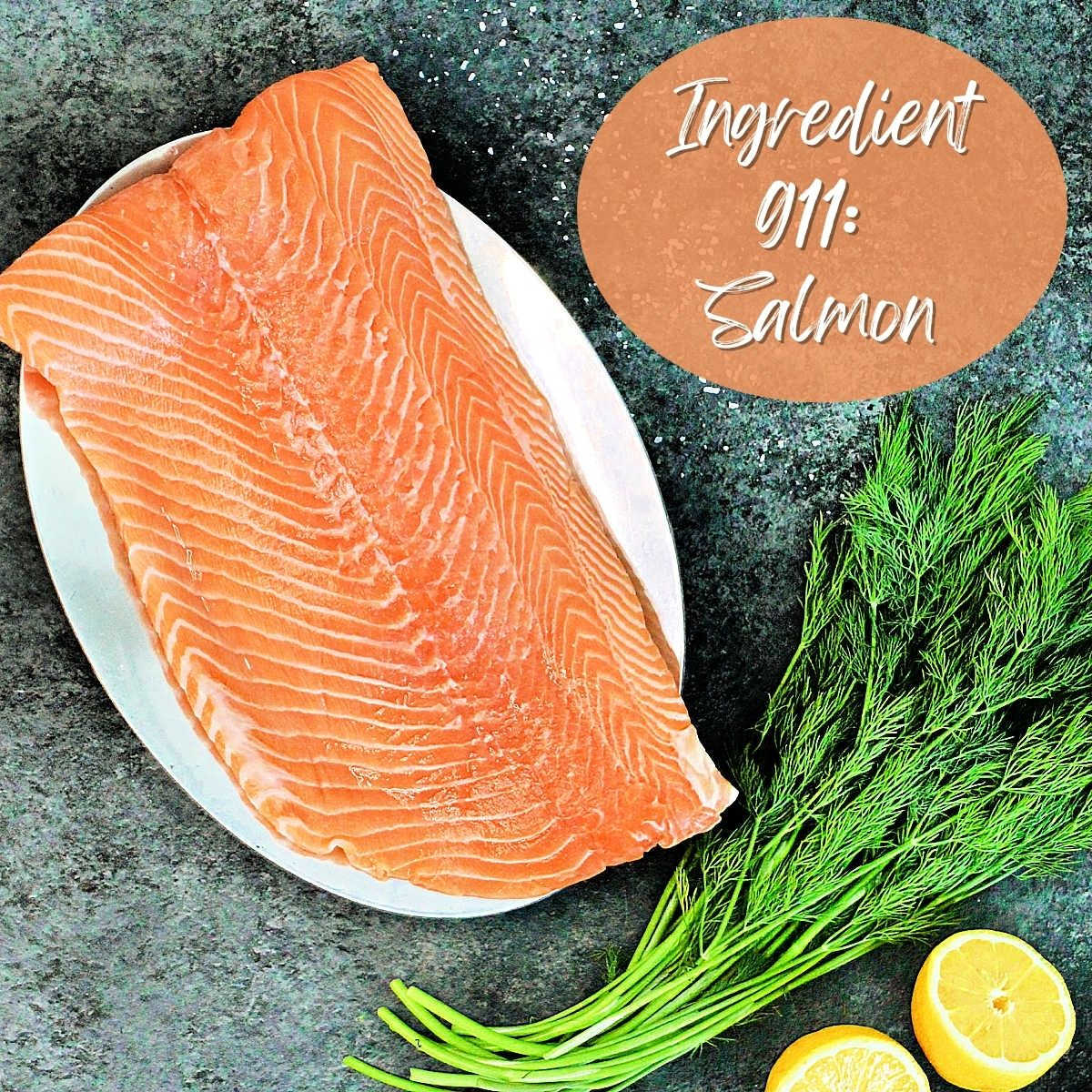 Large piece of salmon on a plate with fresh dill and lemon halves.