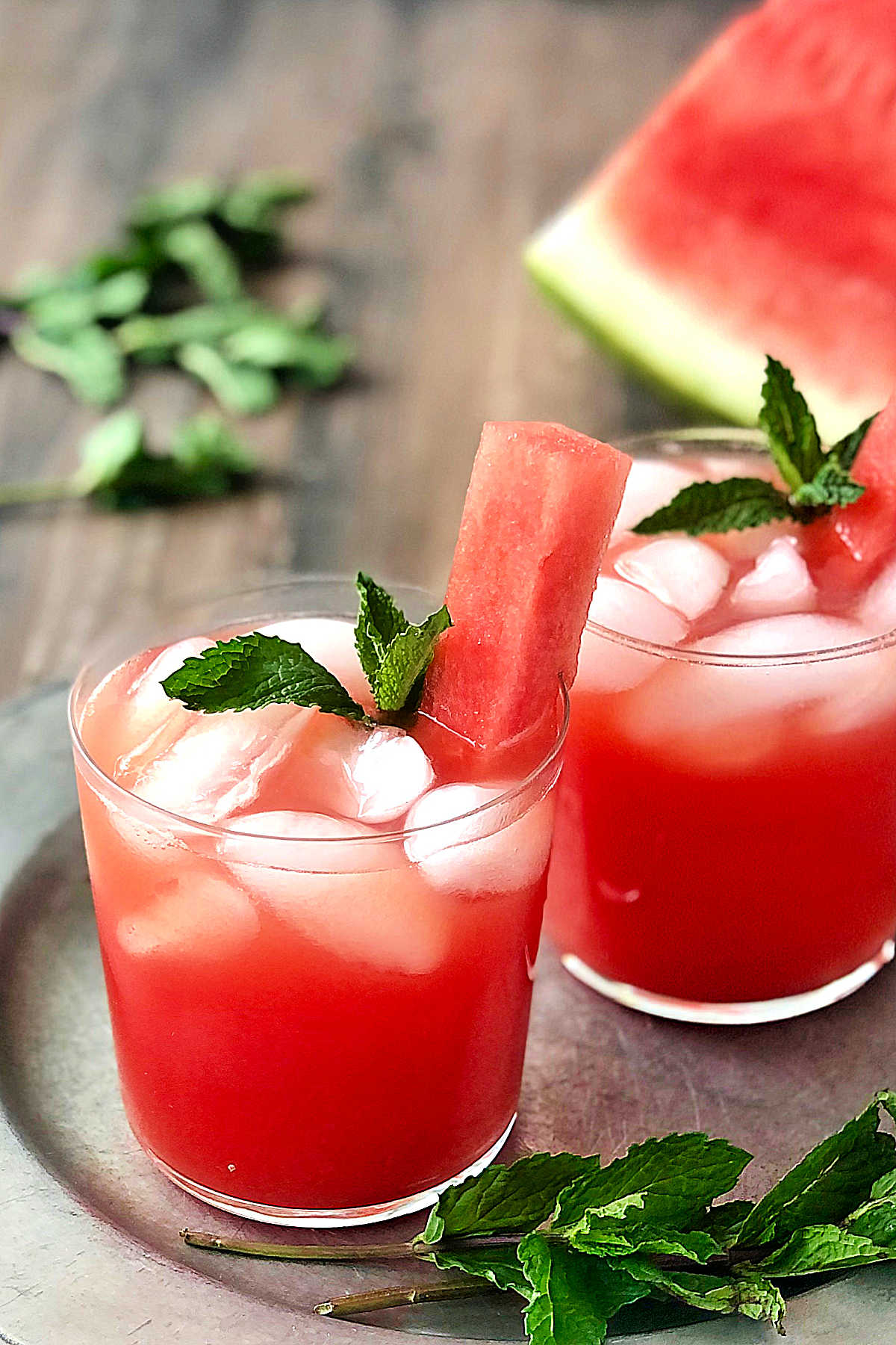 2 glasses of Watermelon Agua Fresca on a silver plate with mint leaves scattered around them.