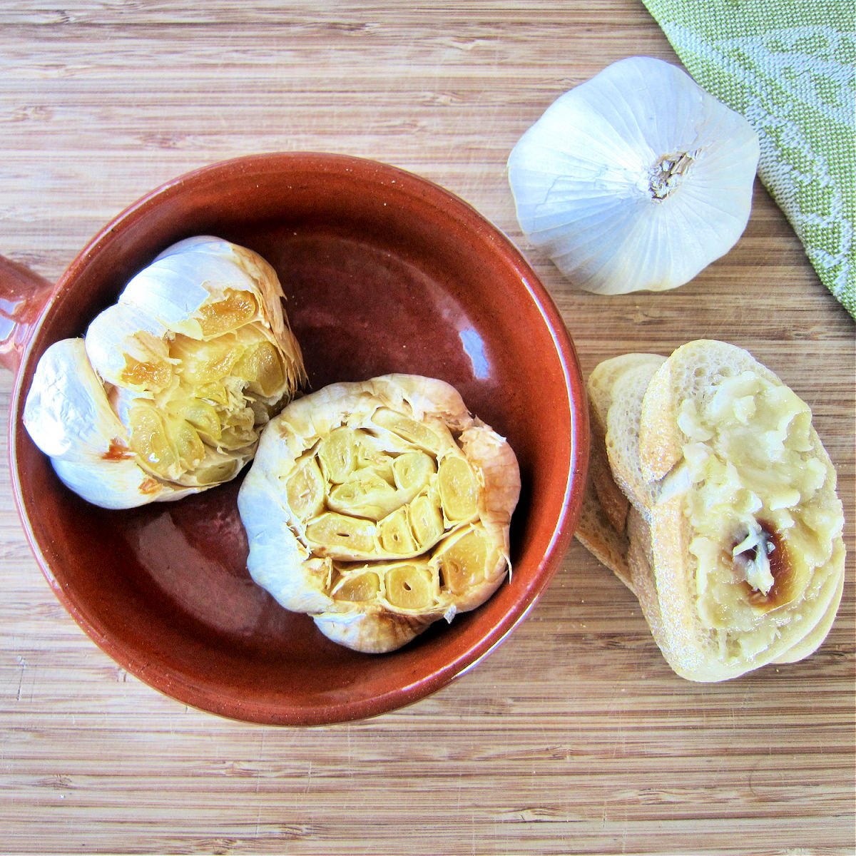 Roasted garlic in a bowl next to toasted with roasted garlic spread on top