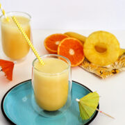 Pineapple banana smoothie on a blue plate with a yellow and white striped straw.