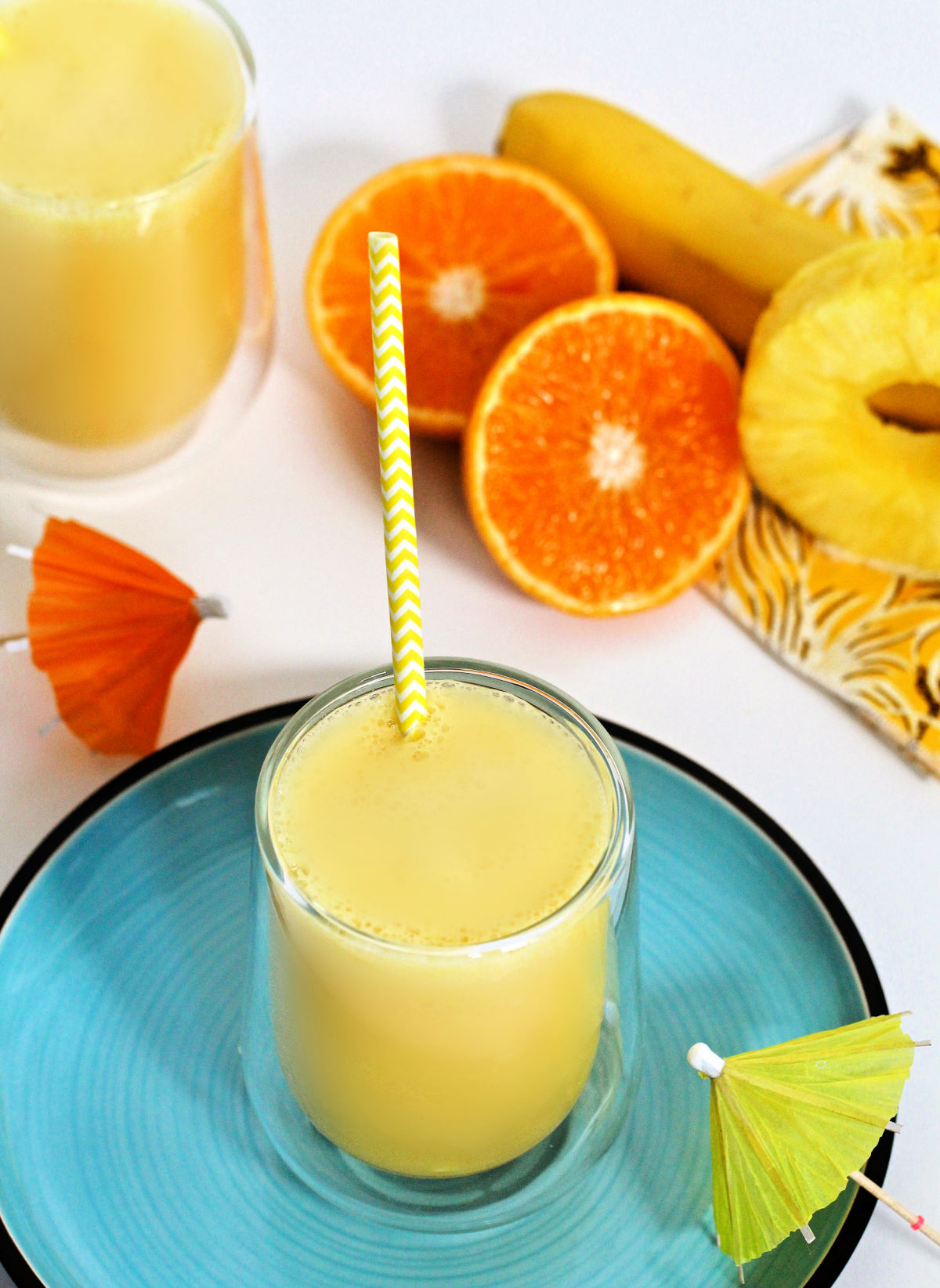 Overhead shot of pineapple banana smoothie on a blue plate with a yellow and white striped straw.