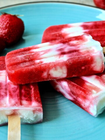 Four Strawberry Greek yogurt popsicles on a blue plate.