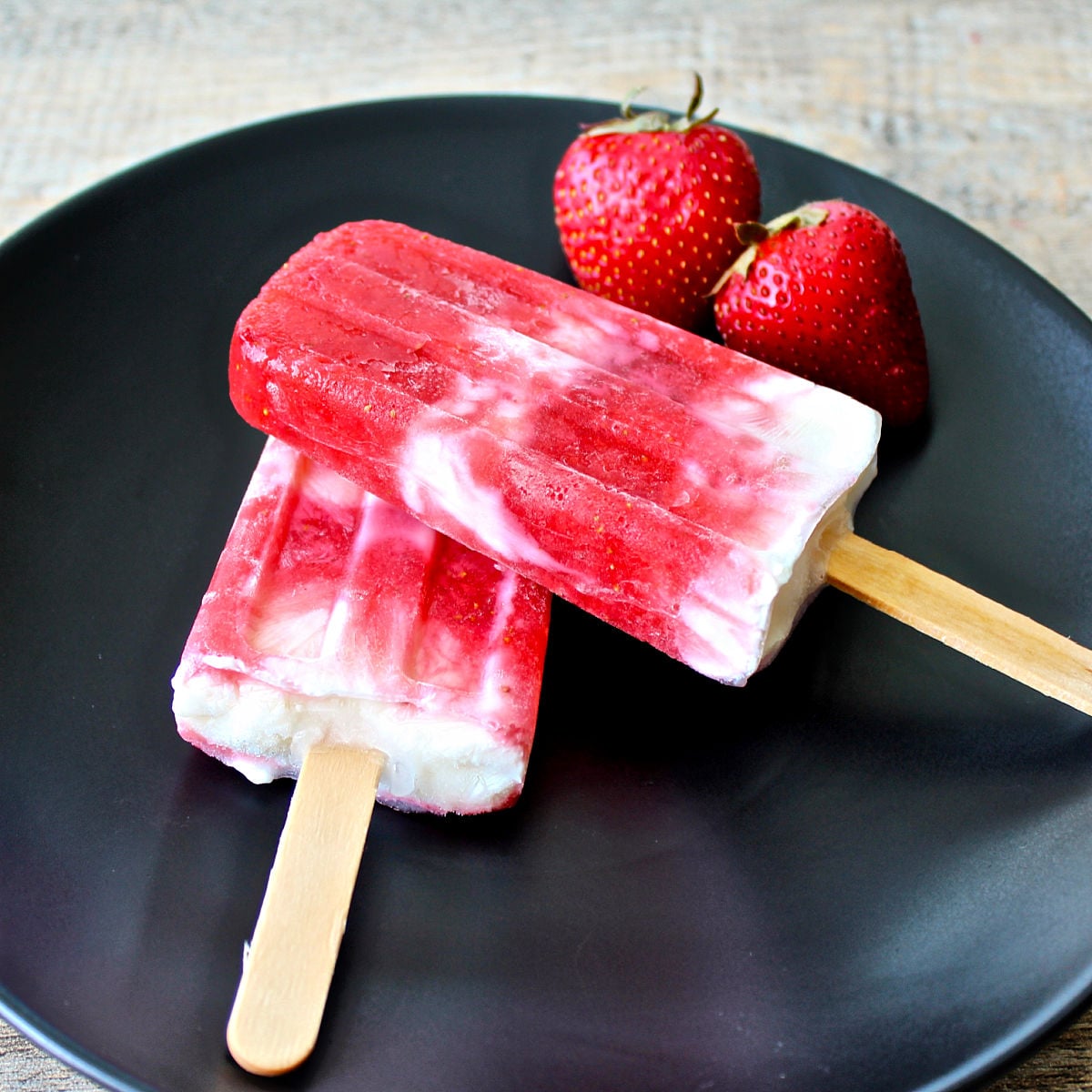 Two Strawberry Greek yogurt popsicles on a black plate.