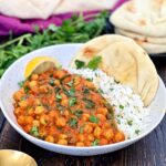 A white bowl with chickpea spinach curry and white rice with naan bread.