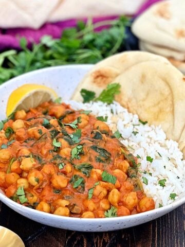 A white bowl with chickpea spinach curry and white rice with naan bread.