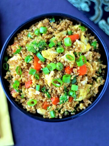 Quinoa fried rice in a black bowl with chopsticks and a yellow napkin nearby.