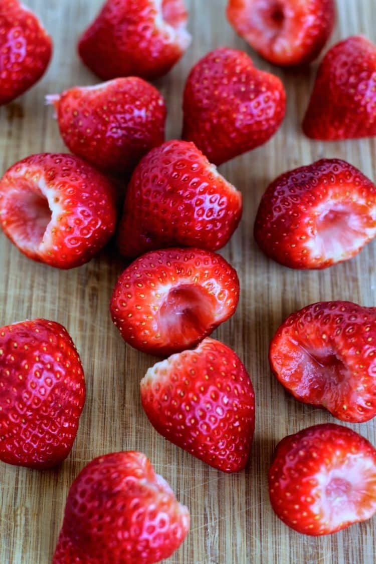 Hulled strawberries on a cutting board.