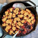 Blueberry peach cobbler in a cast iron skillet with two spoons.