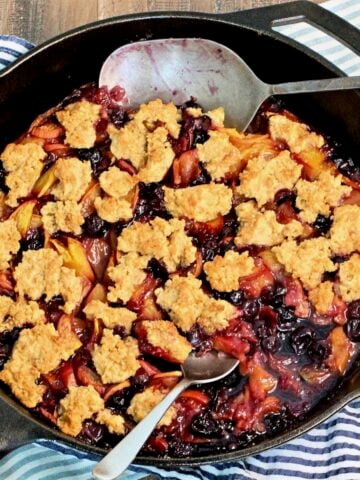 Blueberry peach cobbler in a cast iron skillet with two spoons.