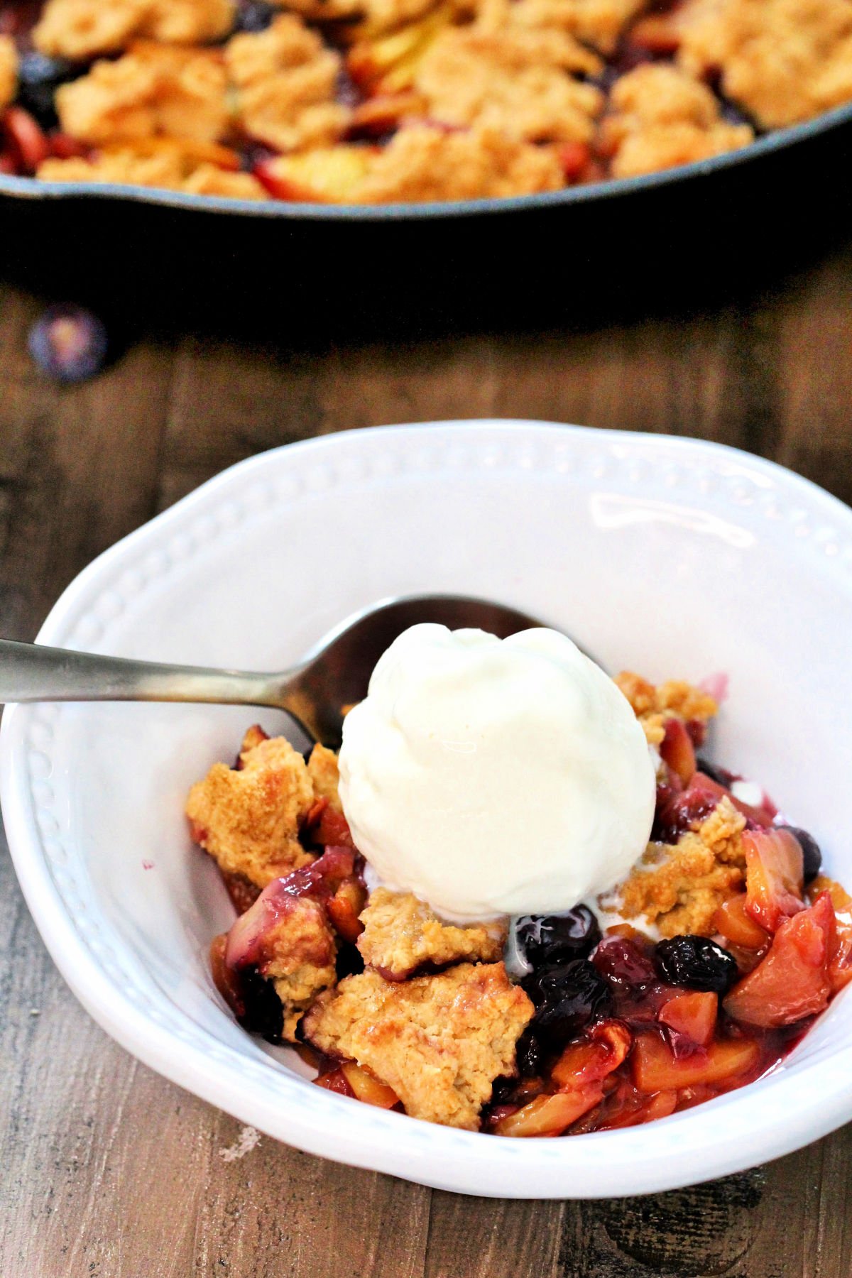 Blueberry Peach Cobbler in a white bowl with a scoop of vanilla ice cream.