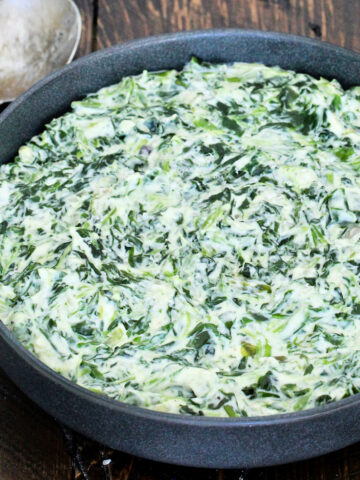 Easy creamed spinach in a black bowl on a wooden board with a metal spoon next to it.