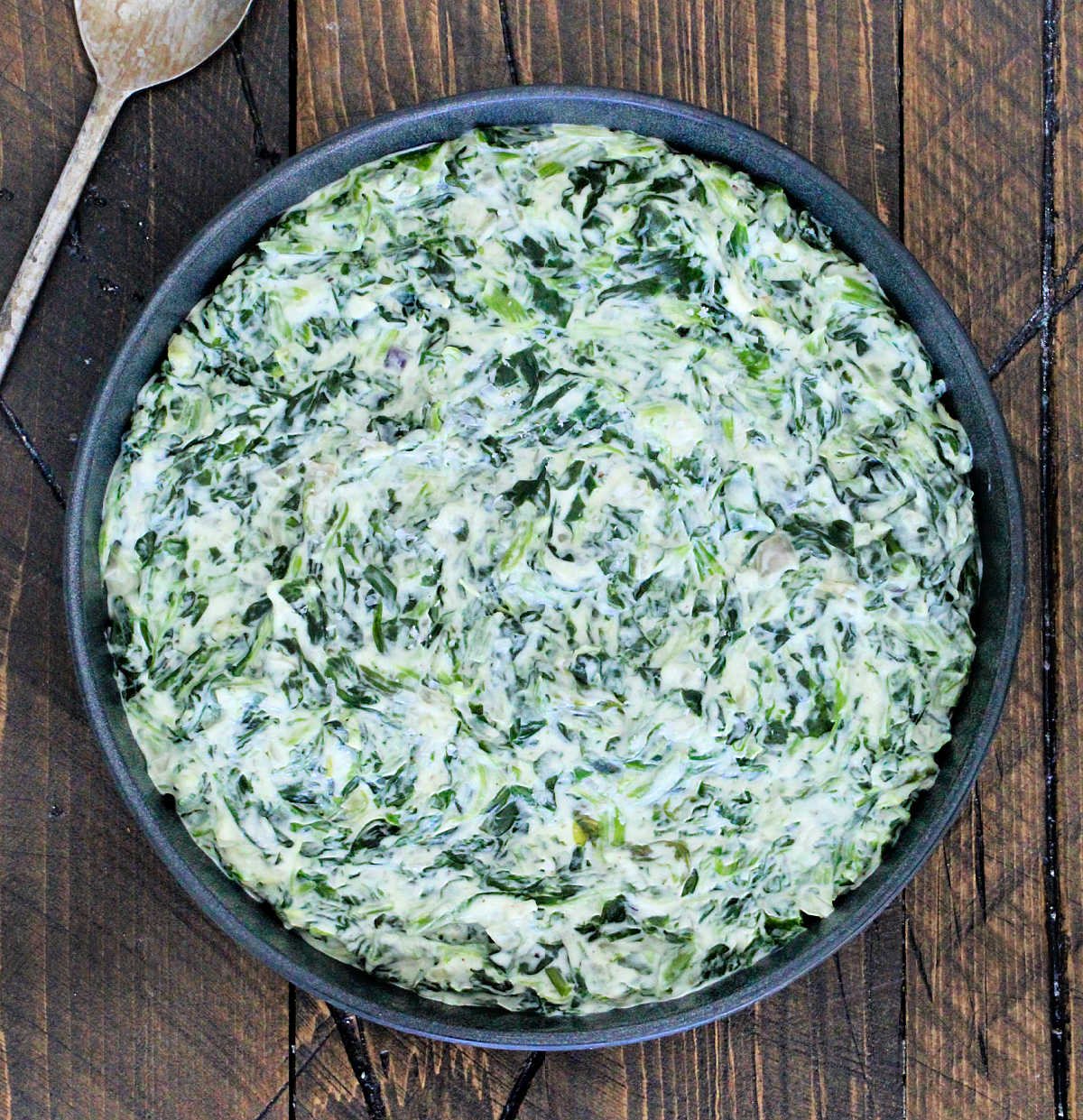 Easy creamed spinach in a black bowl on a wooden board with a metal spoon next to it.