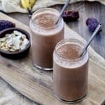 Two healthy chocolate smoothies in glasses with metal straws in them.