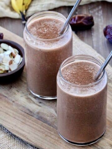 Two healthy chocolate smoothies in glasses with metal straws in them.