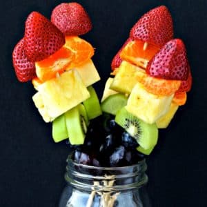 Rainbow fruit kabobs in a mason jar with a black background..