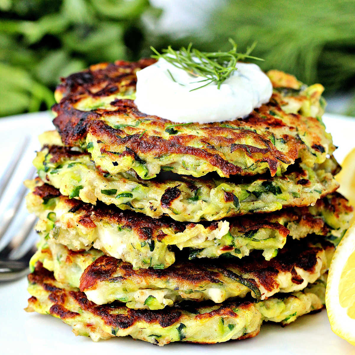 Stack of zucchini fritters with a dollop of yogurt on top.