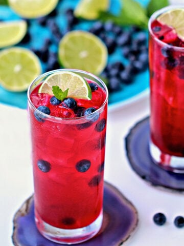 2 glasses of blueberry mint limeade garnished with fresh blueberries and lime slices.