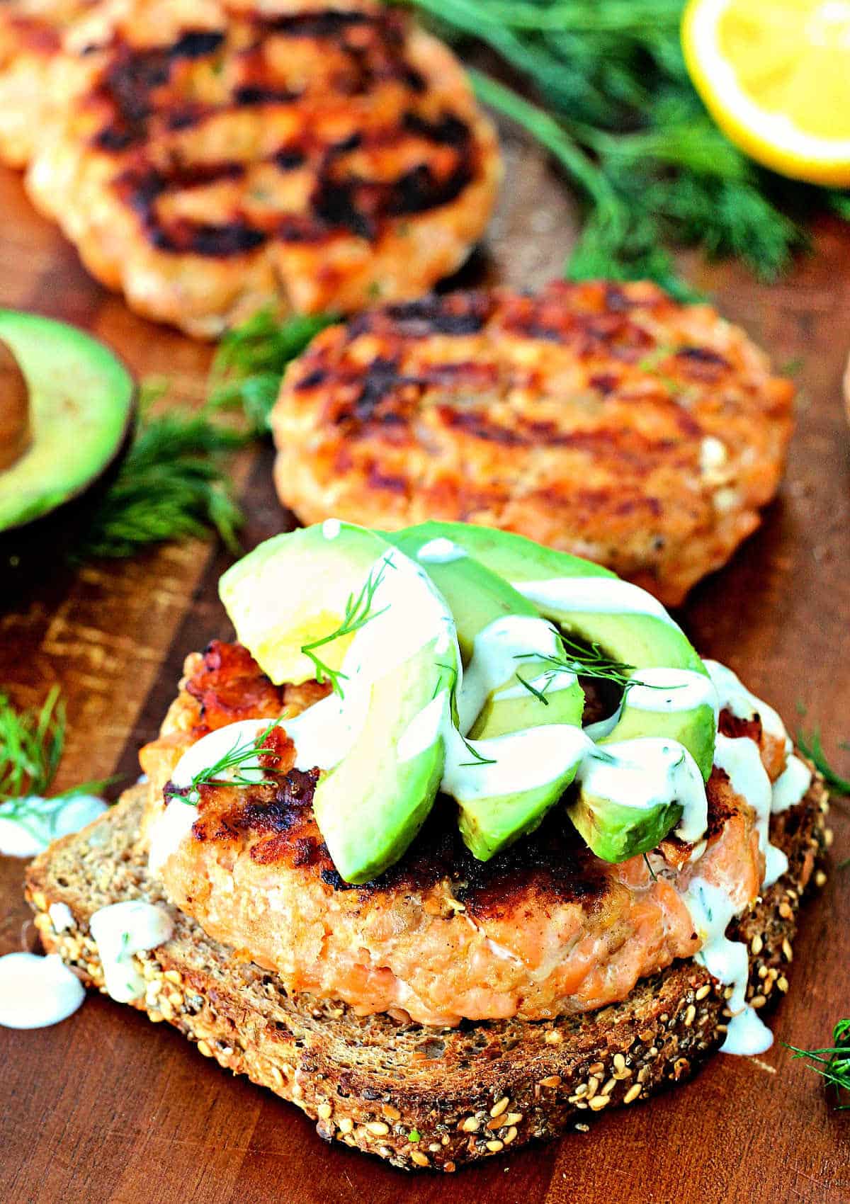 Grilled salmon burger on a piece of toast with avocado slices and dill yogurt sauce on top.