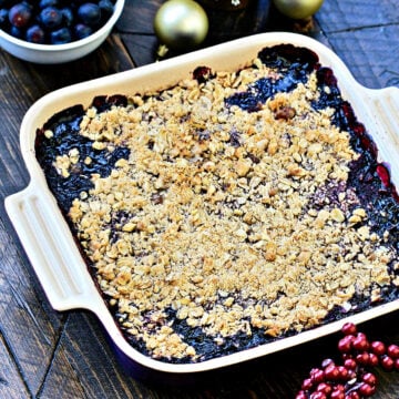 Angled photo of blueberry crisp in a square baking dish with holiday decorations.