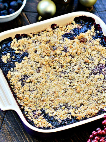 Angled photo of blueberry crisp in a square baking dish with holiday decorations.