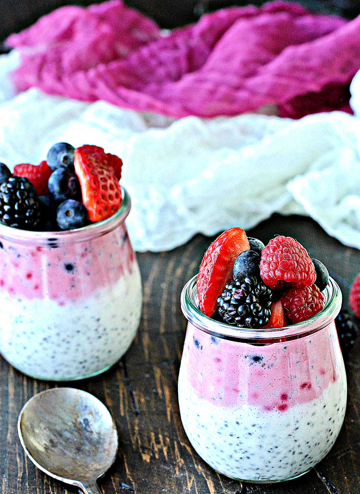 Two mason jars with berry chia pudding topped with fresh berries.