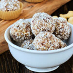 Coconut date balls in a white bowl with a wooden board in the background.