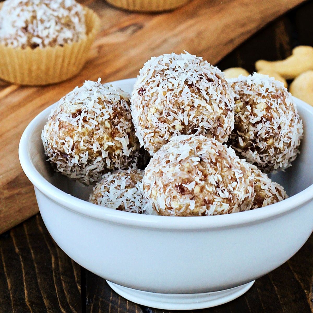 Coconut date balls in a white bowl with a wooden board in the background.