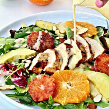Creamy citrus salad dressing being poured onto salad on a white plate.
