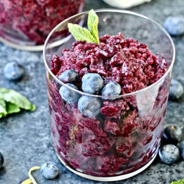 blueberry granita in a glass garnished with blueberries and mint sprig.