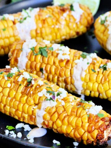 Four pieces of air fryer corn on the cob on a black plate.
