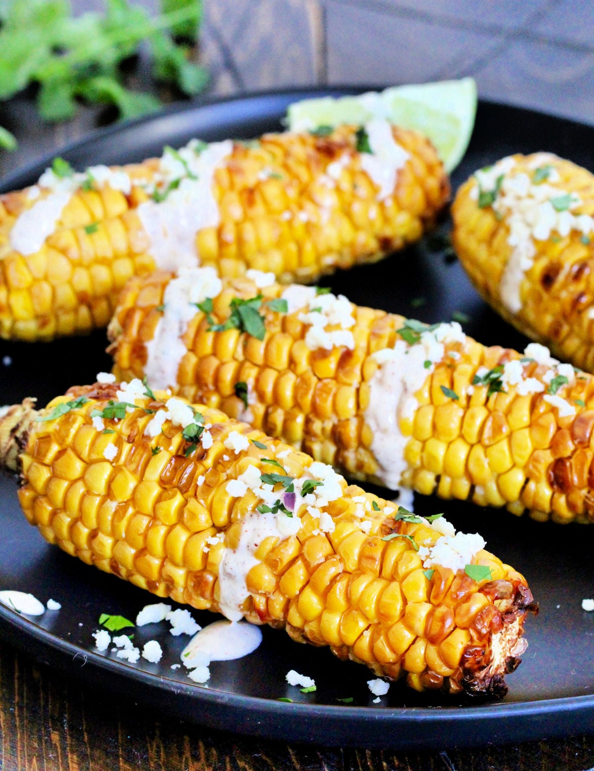 Four pieces of air fryer corn on the cob on a black plate.