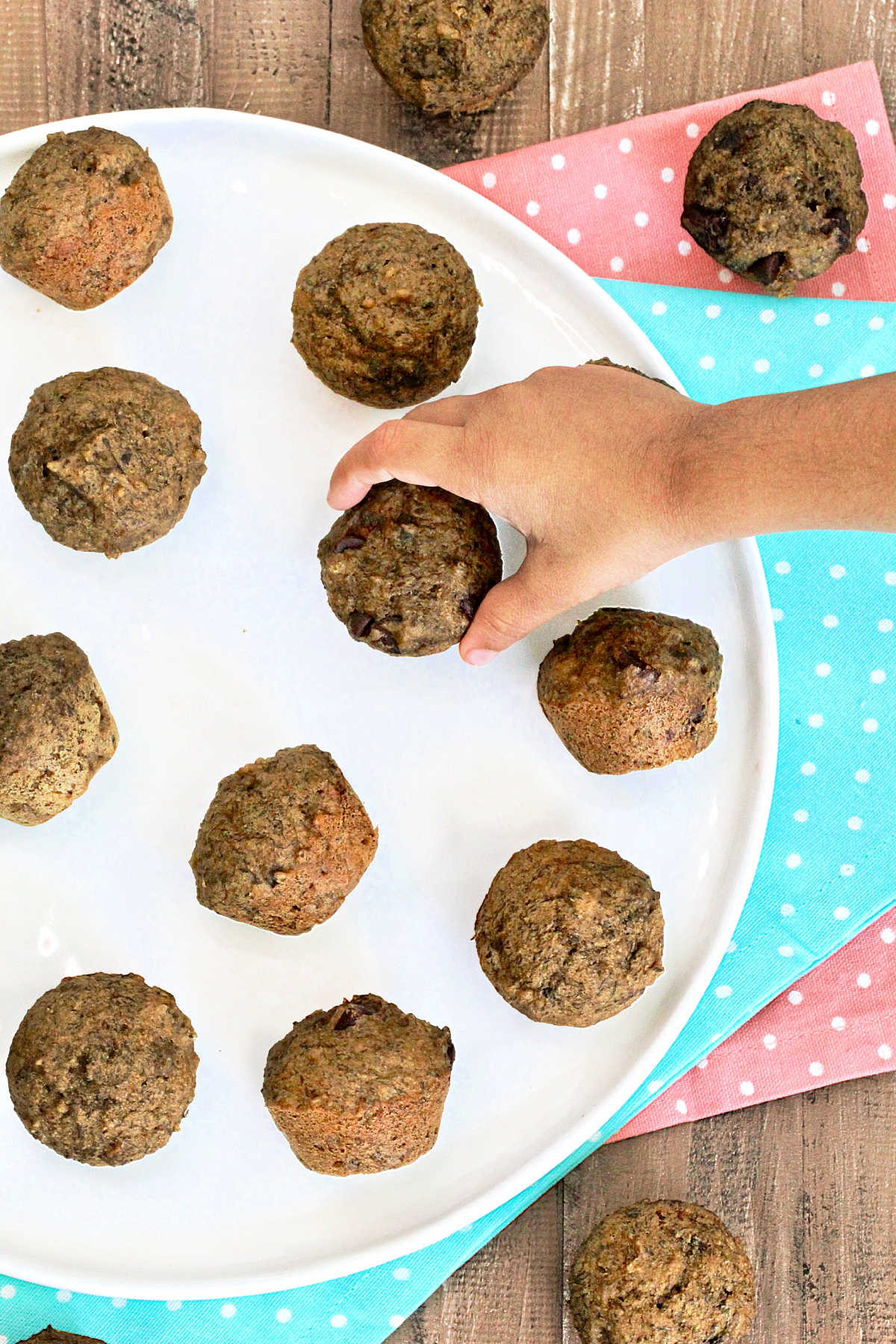 A toddler's hand grabbing a mini banana date muffin from a plate. 
