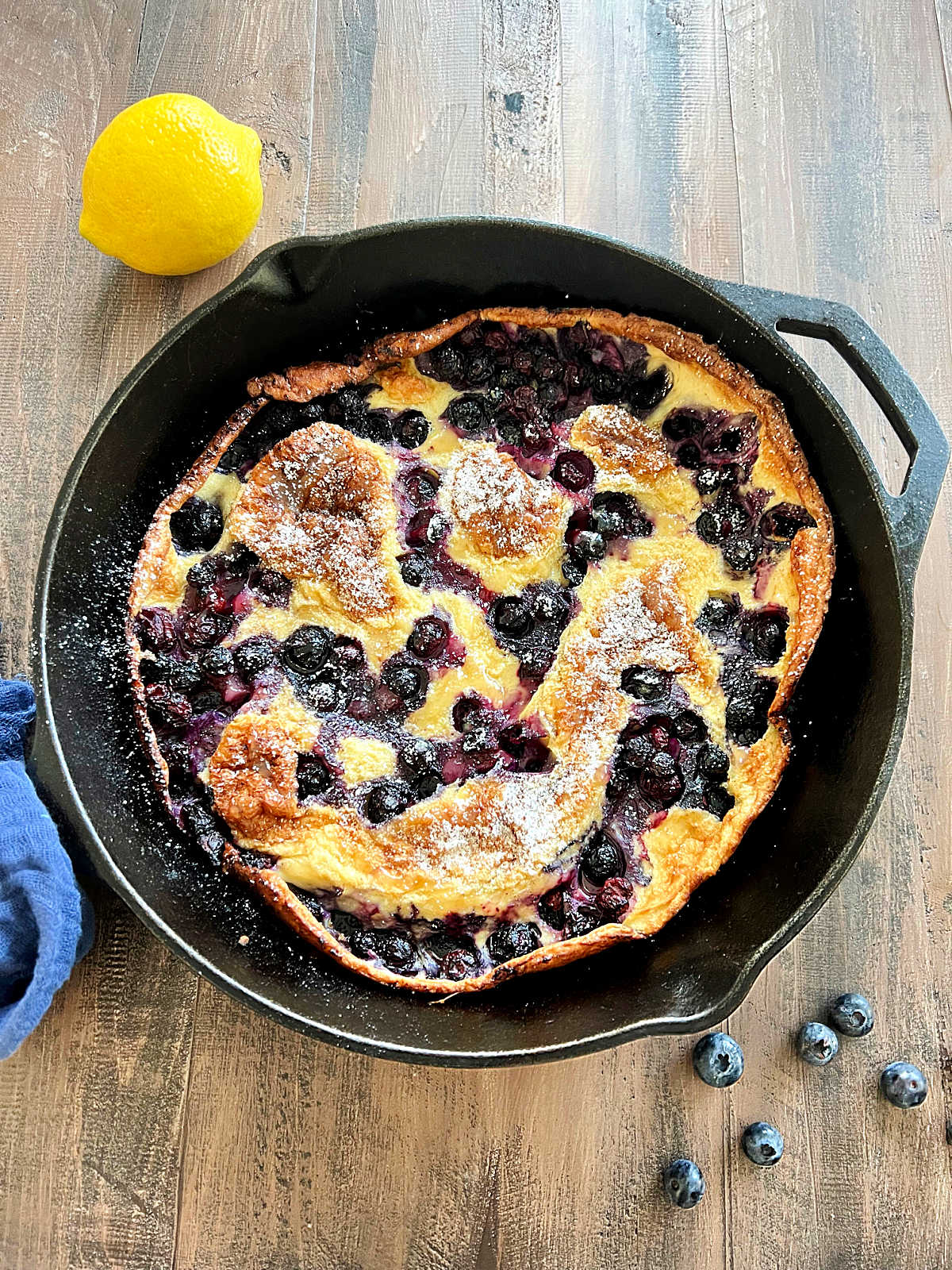Blueberry Lemon Dutch Baby in cast iron skillet on wooden board.