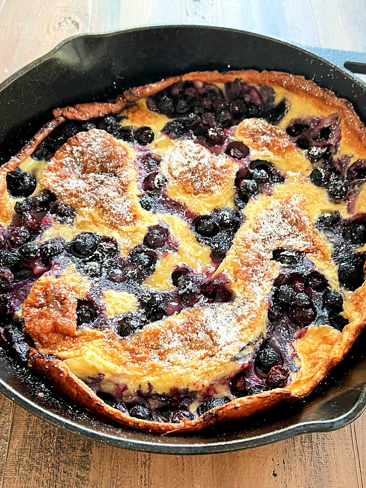 Blueberry Lemon Dutch Baby in cast iron skillet on wooden board.