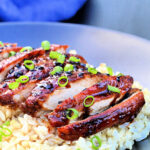 Sliced chicken teriyaki on a bed of brown rice.