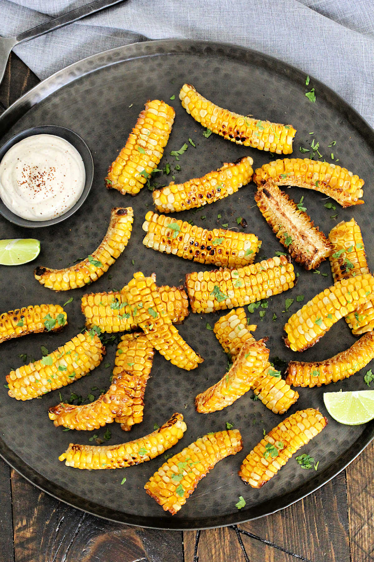 Corn ribs on a bronze platter with lime wedges and Southwest dipping sauce.