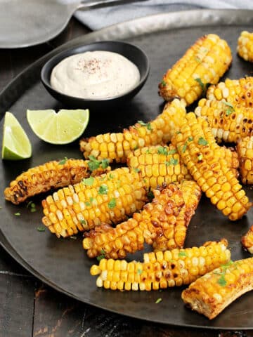 Corn ribs on a bronze platter with lime wedges and Southwest dipping sauce.