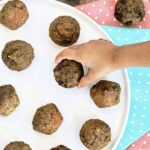 A toddler's hand grabbing a mini banana date muffin from a plate.