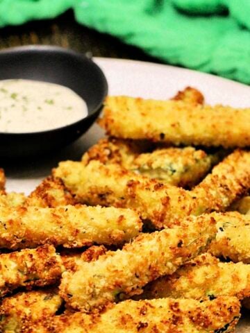 Air fryer zucchini fries on a plate with bowl of ranch dipping sauce and a green napkin.