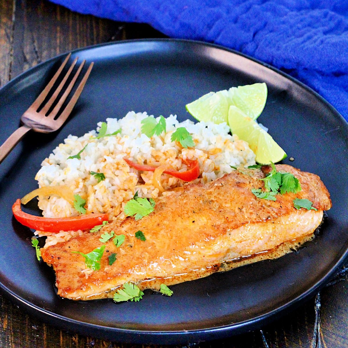 Thai salmon curry on a black plate with a blue napkin next to it