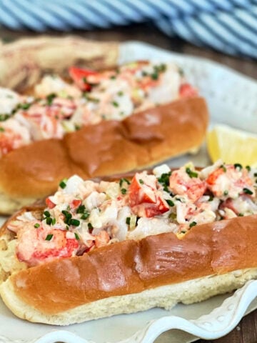 Two lobster rolls on a white plate with lemon wedges.