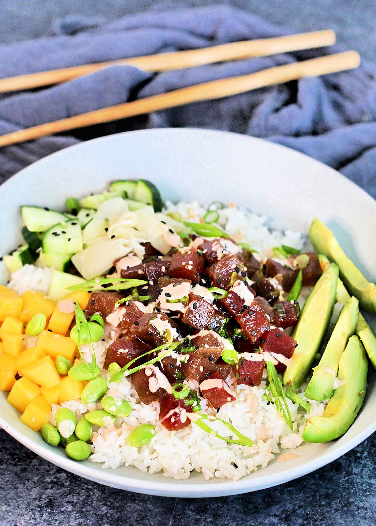 Spicy Tuna Poke Bowl in a white bowl with a gray napkin and wooden chopsticks nearby.