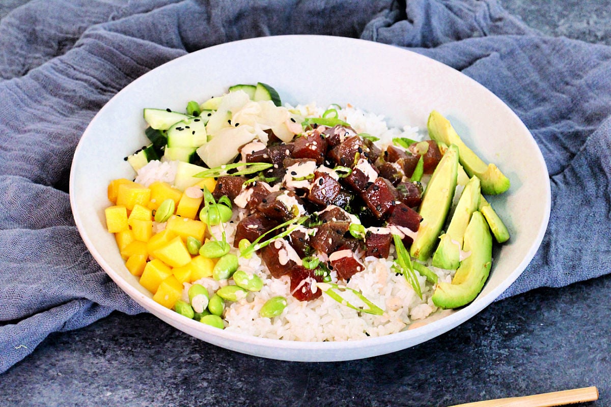 Spicy Tuna Poke Bowl in a while bowl with a gray napkin and wooden chopsticks nearby.