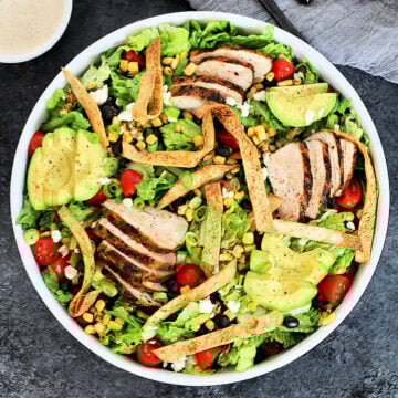 Overhead shot of santa fe salad in a white bowl with a small bowl of dressing on gray board.