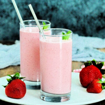 Two glasses of strawberry lassi on a white plate with gray background.