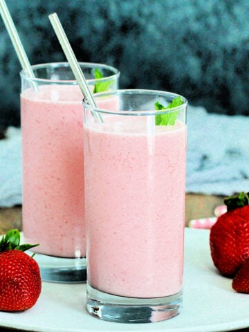 Two glasses of strawberry lassi on a white plate with gray background.