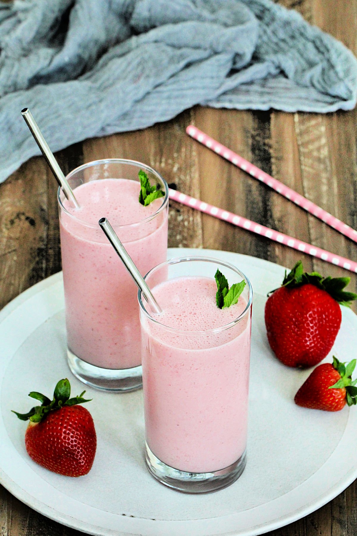 Two glasses of strawberry lassi on a white plate on top of a brown wooden board.