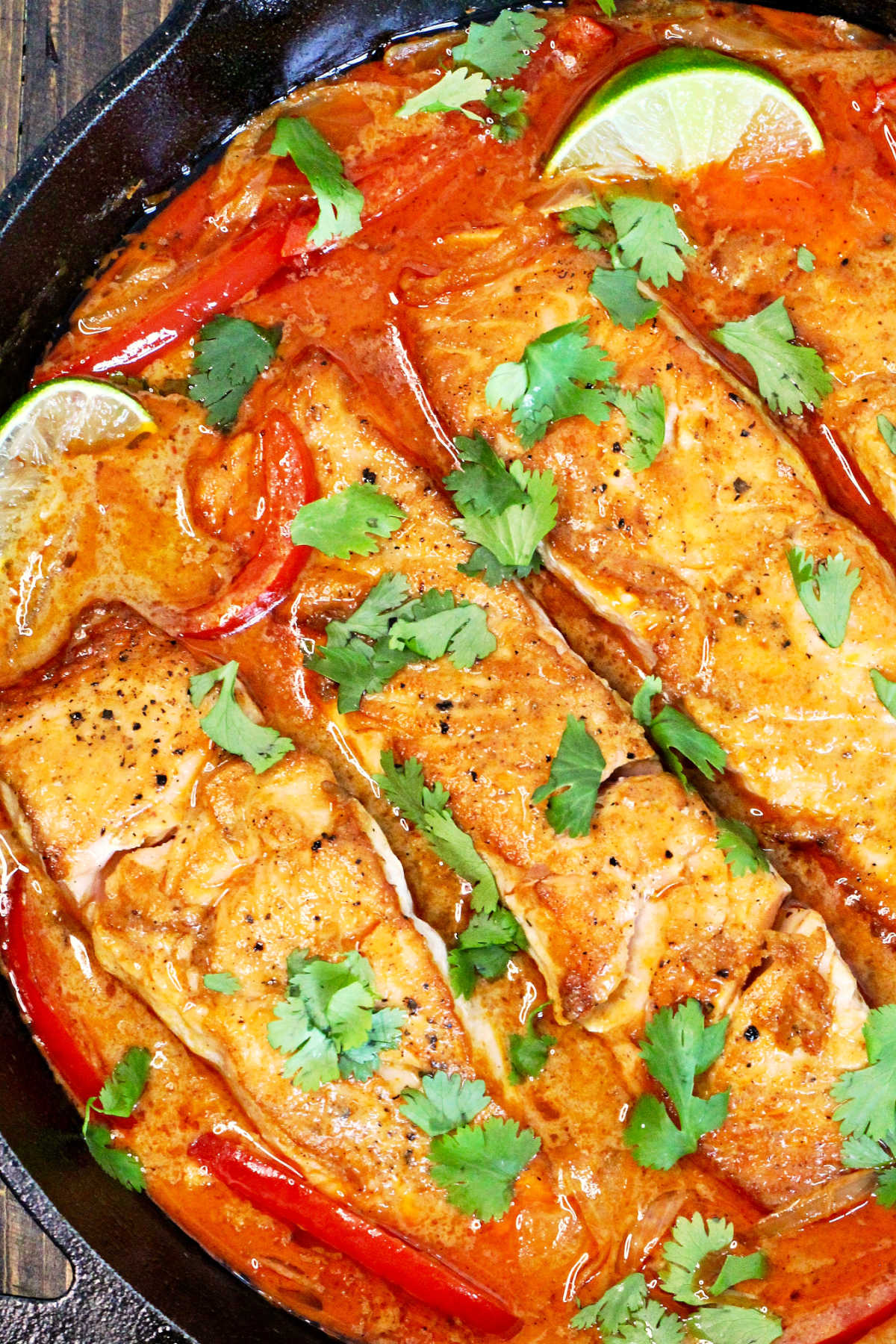 Thai salmon curry in a cast iron skillet on a wooden board